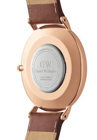 Rose gold watch case with a stainless steel back, brown leather strap, smooth texture, and engraved brand details.
