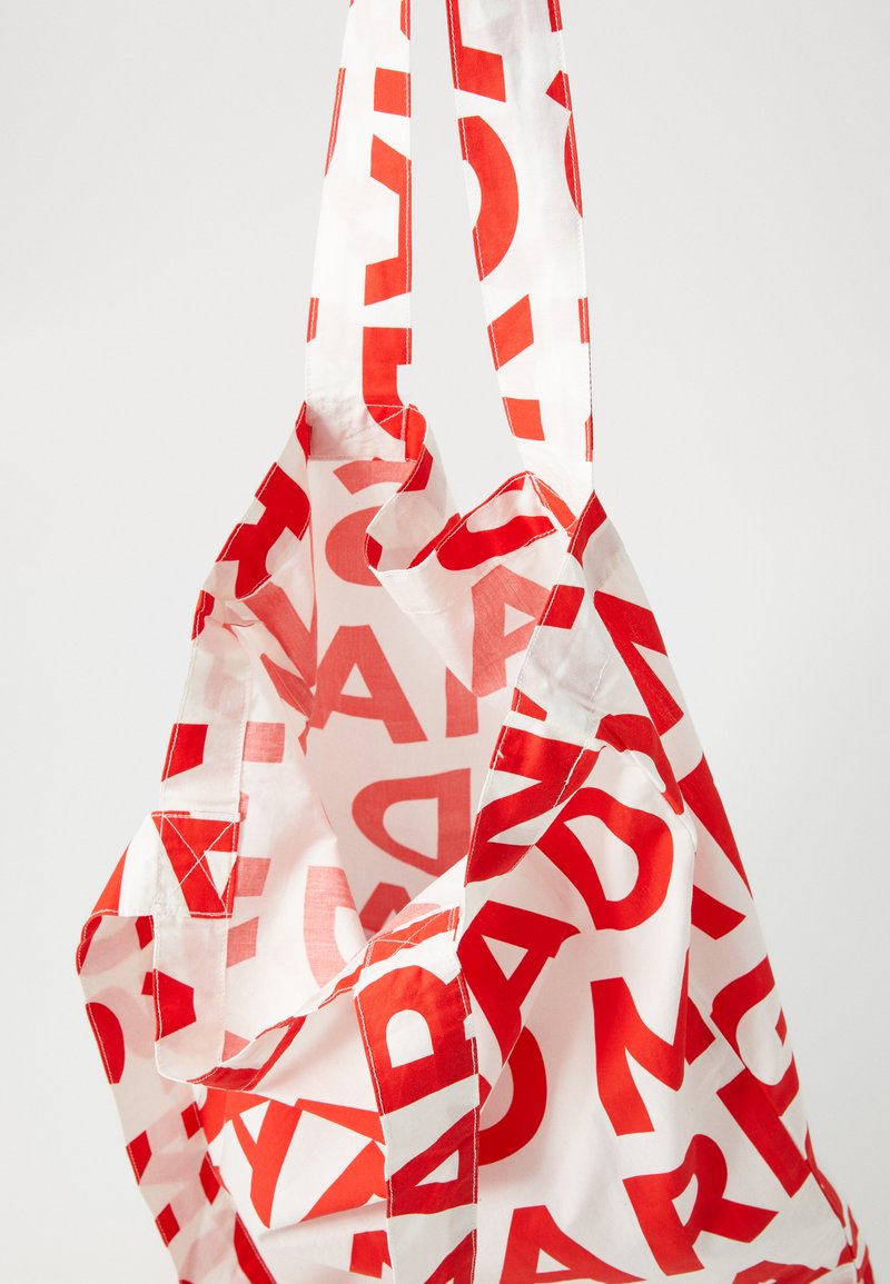 Bolsa de tote reutilizable hecha de tela ligera, con un fondo blanco y un texto rojo destacado. El diseño incluye asas resistentes y acentos cosidos.
