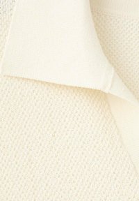 Tejido de punto en beige claro con un patrón texturizado. Presenta un cuello liso y un brillo sutil, que realza el detalle suave del textil.