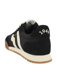 Zapatilla atlética en blanco y negro con parte superior de ante y textil, que presenta una prominente franja blanca, suela de goma y "1949" grabado en el talón.