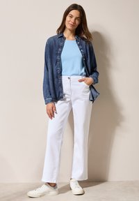 Denim overhemd, lichtblauwe T-shirt, witte wijde broek en witte sneakers. De outfit heeft een relaxte pasvorm en knoopdetails op het overhemd.