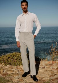 White long-sleeve shirt with a button-up design and vertical stripes, paired with light grey pinstriped trousers and polished black shoes.
