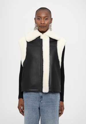 Gilet en cuir noir avec un col et des bordures en fausse fourrure crème. Il présente un design sans manches et des poches à l'avant, avec une texture lisse.