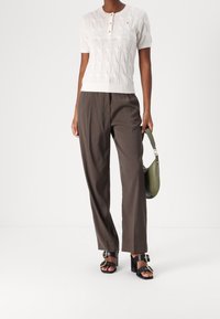 Haut blanc à manches courtes en maille torsadée avec patte de boutonnage, associé à un pantalon marron ample et des sandales noires à talons blocs. Accessoire sac à main vert.