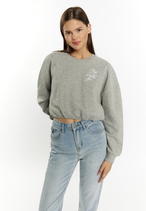 Szary krótki sweatshirt z okrągłym dekoltem i długimi rękawami, z białym haftowanym napisem. W połączeniu z jasnoniebieskimi spodniami z wysokim stanem.