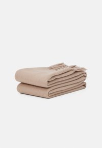 Plaid en laine beige soigneusement plié avec des accents de franges sur un bord. Texture douce avec une finition lisse et uniforme.