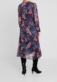 Vestido floral de tela translúcida, con patrones rosas y azules sobre un fondo negro. Destacado por un dobladillo fluido y mangas largas.