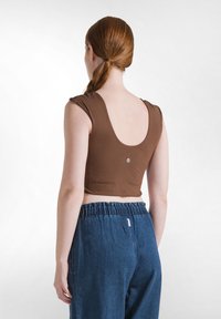 Bruine cropped top met brede halslijn en korte mouwen, gecombineerd met blauwe denim broek met een elastische tailleband en een klein label.