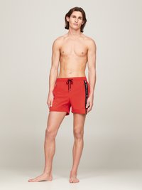 Pantaloni da bagno rossi realizzati in tessuto leggero; presentano un elastico in vita con cordoncino e accenti neri laterali con testo. La lunghezza arriva a metà coscia.
