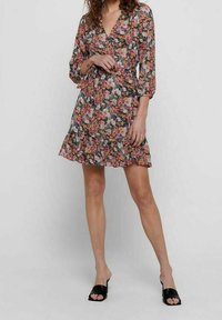 Blumenkleid mit drei Viertel-Ärmeln, lebhaften Mustern in Pink, Grün und Weiß. Es hat einen rüschengesäumten Saum und einen tiefen V-Ausschnitt.
