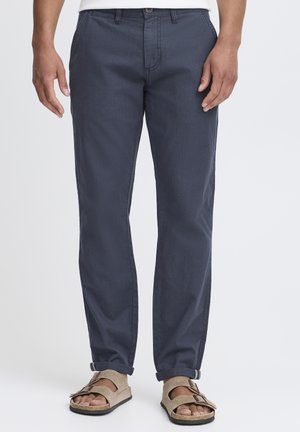 Chinos bleus marine pour homme en coton, avec une coupe droite, des poches avant et des poignets retroussés, associés à des sandales beiges.