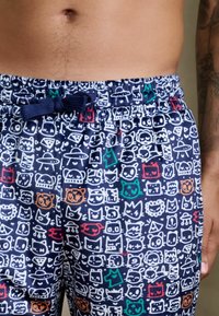 Bawełniane kąpielówki w granatowym kolorze, ozdobione zabawnym białym wzorem graficznym twarzy i kształtów, z elastyczną talią i sznurkiem do regulacji.