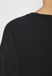 Camiseta de algodón negra con cuello redondo y detalles de costura sutiles, que destacan una textura suave y uniforme.
