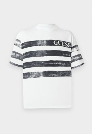 Fehér pamut póló vízszintes fekete csíkokkal, megviselt textúrával és vastag fekete "GUESS" logóval az elején.