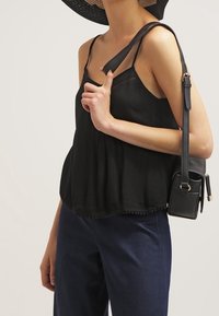 Woman wearing a black sleeveless top, navy pants, large black hat, and carrying a black leather shoulder bag.