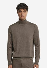 Brauner Rollkragenpullover aus weichem Strickmaterial, mit eng anliegenden Ärmeln und geripptem Kragen, im lässigen Schnitt gestaltet.