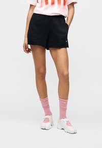 Μαύρο αθλητικό σορτς με ελαστική μέση, συνδυασμένο με ροζ ριμπ κάλτσες και λευκά αθλητικά παπούτσια. Το σορτς διαθέτει πλαϊνές τσέπες.