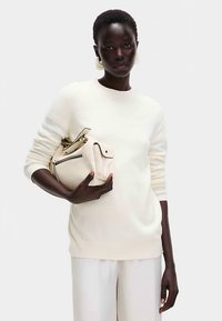 Krämfärgad stickad tröja med ribbstickade ärmslut, kombinerad med en strukturerad offwhite handväska med dragkedjor och klaffstängning.