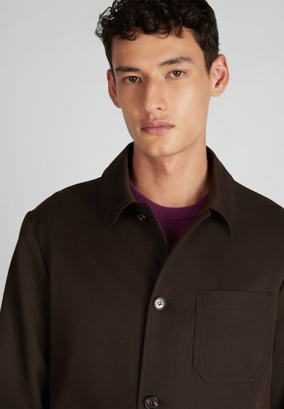 Brązowa kurtka zapinana na guziki z kołnierzykiem, wykonana z teksturowanej tkaniny, z kieszenią na lewej piersi i kontrastującą wewnętrzną warstwą.