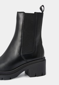 Zwarte leren Chelsea-laars met elastisch zijpaneel, stevige hak en een rubberen zool met structuur en opvallende uitsparingen.