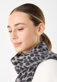 Sciarpa con stampa leopardata grigia e nera, realizzata in tessuto morbido, avvolta attorno al collo, con una texture liscia e una caduta casuale.