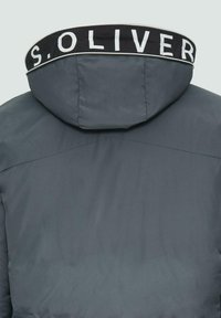 Grijze hoodie-jack met een gestructureerde afwerking, voorzien van een zwarte kraag met witte letters. Gladde stof en minimale ontwerpelementen.