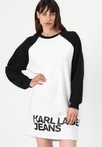 Vestido de sweatshirt branco com mangas raglan negras. Apresenta um audacioso texto "KARL LAGERFELD JEANS" na barra. Ajuste suave e casual.