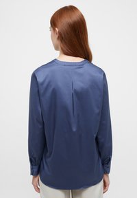 Marineblå langærmet bluse i satinfinish med rund halsudskæring, rygfoldsdetalje og knapmanchetter. Glat tekstur og afslappet pasform.