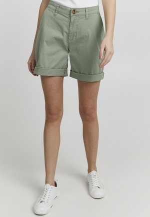 Lichtgroene katoenen shorts met opgerolde mouwen, een sluiting met voorknop en zijzakken. Gepaard met witte veterschoenen.