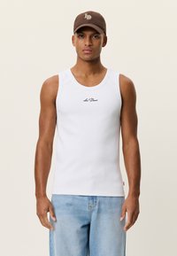 Débardeur blanc à texture lisse et encolure ronde, orné d'un petit logo noir. Associé à un short en denim bleu clair.