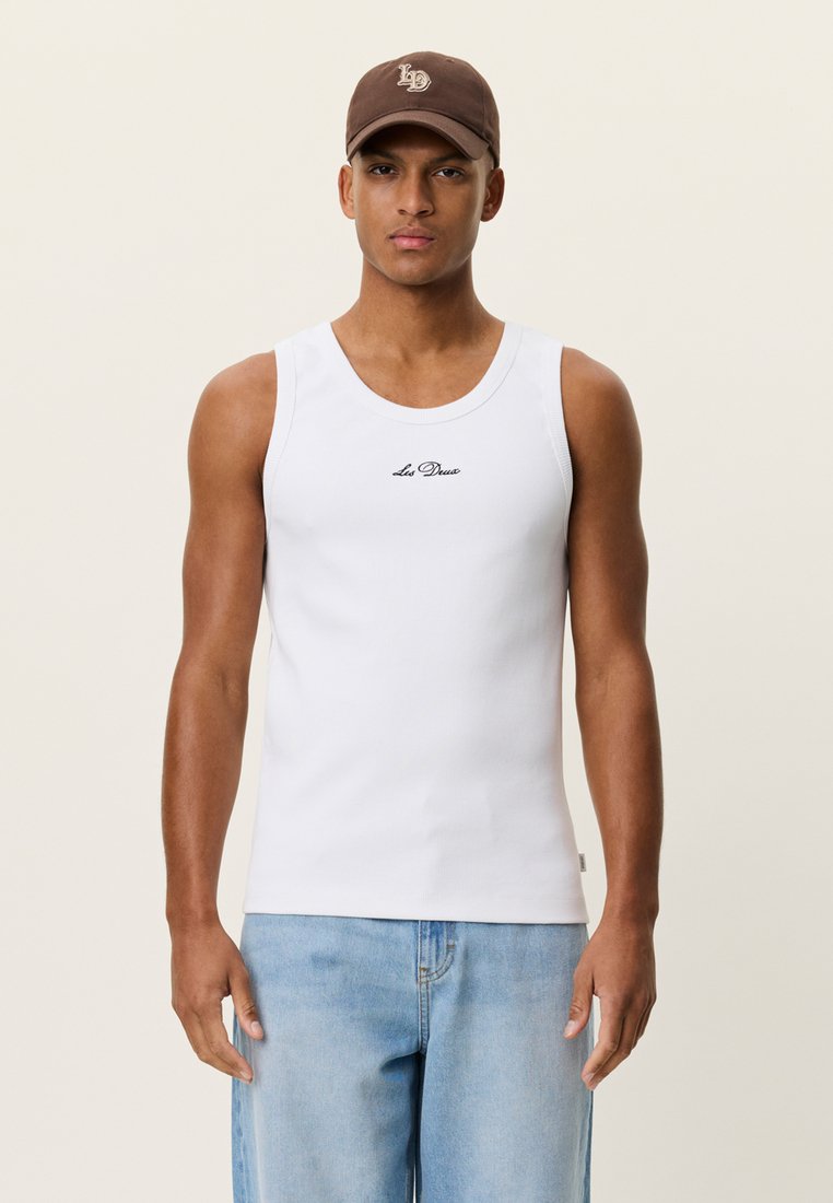 Débardeur blanc à texture lisse et encolure ronde, orné d'un petit logo noir. Associé à un short en denim bleu clair.