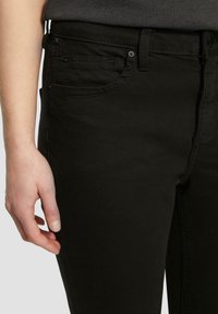 Czarne dżinsy o slim fit, z pięcioma kieszeniami i gładką teksturą. Widoczne szwy wzdłuż szwów.