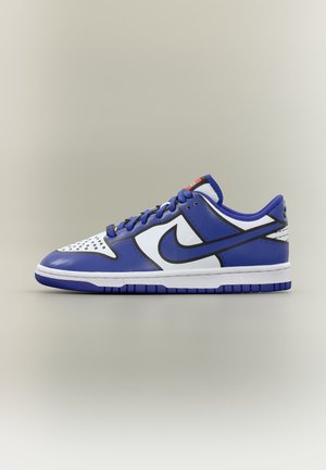 Baskets basses bleu et blanc avec virgule noire Nike, semelle blanche, lacets bleus et contours noirs façon dessin animé sur fond neutre.