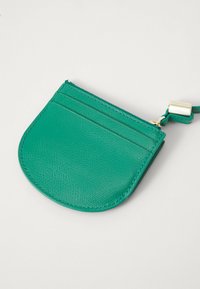 Green leather cardholder with a rounded shape, textured surface, and three card slots; features a gold zip and a detachable strap.