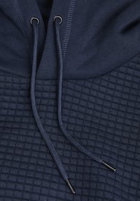 Marineblaue Kapuzenjacke mit einem strukturierten, gesteppten Muster, versehen mit Kordelzügen und metallenen Enden. Weicher Stoff und verstärkte Nähte.