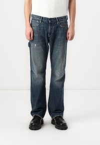 Jeans de ganga azul escuro com um corte regular, apresentando desgastes leves, cinco bolsos e um design de perna reta.