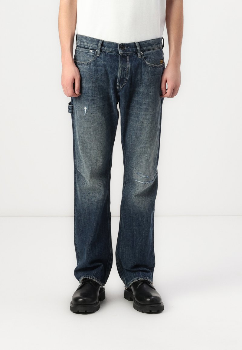 Jeans de ganga azul escuro com um corte regular, apresentando desgastes leves, cinco bolsos e um design de perna reta.