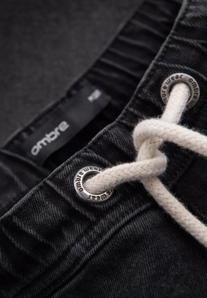 Shorts in denim nero con cintura elastica, caratterizzati da un laccio intrecciato bianco e occhielli in metallo impressi con "ombre wear."