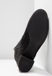 Botín negro de ante con suela de goma texturizada, cremallera lateral y diseño minimalista; cuenta con un tacón bajo y un acabado suave.