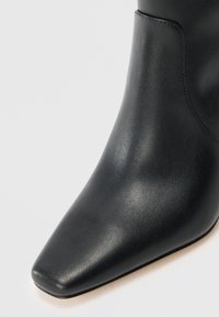 Stivale alla caviglia in pelle nera con punta appuntita, texture liscia e silhouette elegante. Caratterizzato da un design minimalistico e senza hardware visibile.