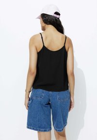 Haut sans manches noir avec de fines bretelles associé à un short en denim bleu. La tenue est conçue pour un usage décontracté avec une coupe décontractée et un style simple.