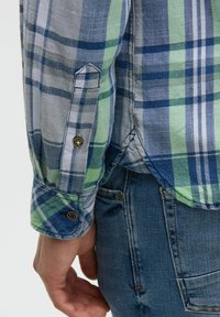 Kurzarmige karierte Hemd in Blau, Grün und Grau. Mit rundem Kragen und Knopfmanschetten; der Stoff ist leicht und strukturiert.