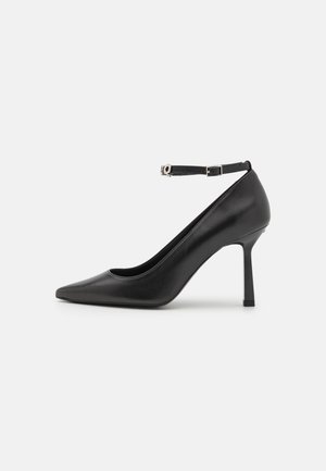 Escarpin noir en cuir avec un bout pointu et une bride à la cheville. Texture lisse, silhouette élégante, et talon aiguille.