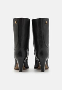 Mustat nahkaiset nilkkurit, joissa on kapea korko, kultainen logovivahde sivulla ja sileä, tyylikäs pinta.