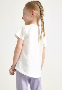 Vit bomulls t-shirt med korta ärmar, rund halsringning och en avslappnad passform, kombinerad med ljuslila leggings. Pärlarmband på handleden.