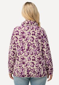 Kremi floralipullover, jossa on violetteja kukkia, korkea kaulus, pitkät hihat ja rento malli. Pehmeä, teksturoitu kangas.
