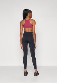 Bordeaux sportsbh og svarte leggings. Leggingsene har perforerte detaljer. Glatt materiale, tettsittende design. Egnet for trening.