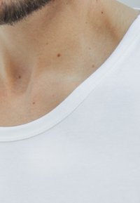 Weißes Baumwoll-T-Shirt mit Rundhalsausschnitt, glatter Textur und sichtbaren Nähten entlang des Kragens und der Schulterpartie.