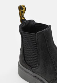 Bottines Chelsea en cuir noir avec un côté en maille texturée, une semelle en caoutchouc épaisse et une languette jaune pour un enfilage facile.