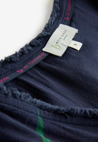 Tumši zila blūze ar noplīsušu apkakles malu un etiķeti. Audums ir mīksts un gluds, ar smalkiem zaļiem akcentiem. Redzama S izmēra etiķete.